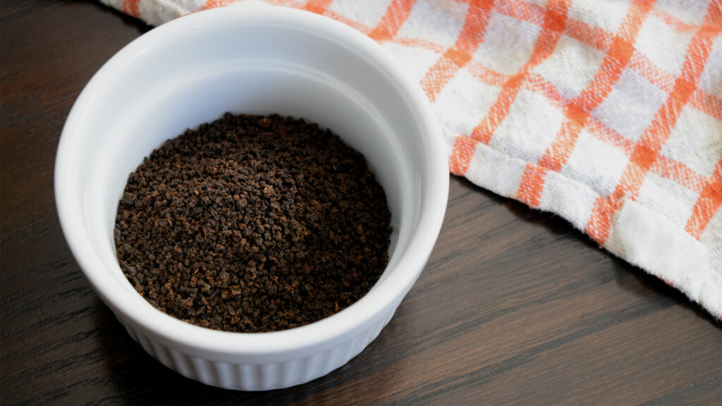 A closeup image of CTC black tea granules in a white ramekin. 