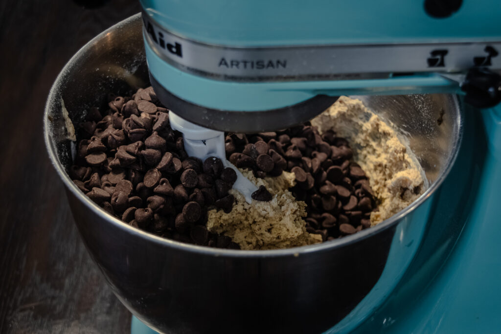 Chocolate chips being added to cookie dough in a stand mixer