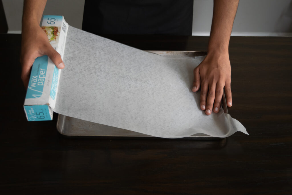 A person lining a baking sheet with parchment paper